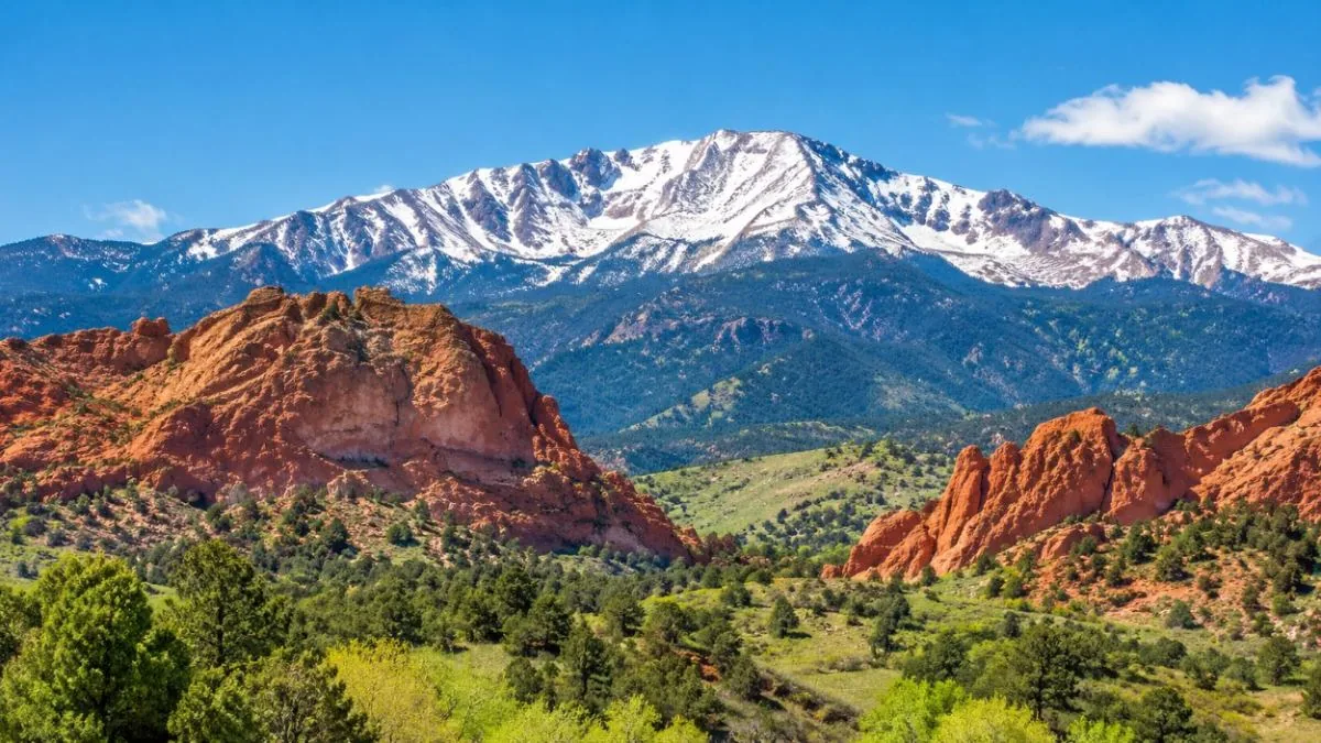 Il Pikes Peak innevato che si staglia dietro rocce rosse e colline verdi